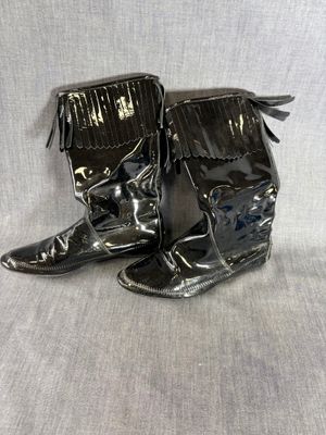 une paire de bottes en cuir noir ornées de franges, posées sur une surface blanche