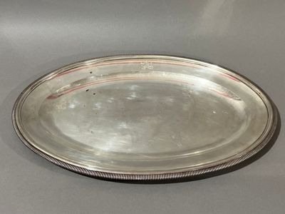 an oval silver plate with a beaded edge on a gray surface