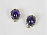 une paire de boucles d'oreilles à clous en verre violet posées sur une surface blanche