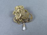 an image of a gold broochle with a woman holding a pearl