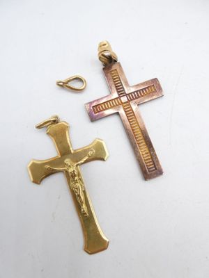 two cross pendants on a white surface with a gold chain