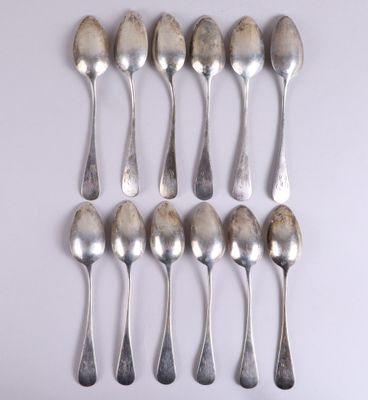 six cuillères en argent sont disposées en ligne sur une surface blanche