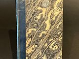 an old book with a black cover sitting on top of a table