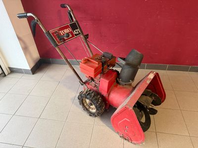 une déneigeuse rouge posée par terre devant un mur rouge