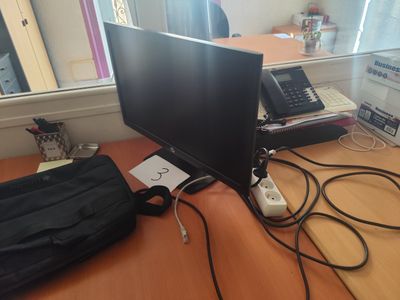 un écran d'ordinateur posé sur un bureau, à côté d'un sac