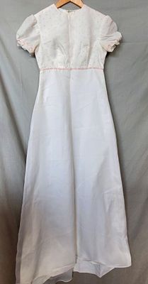white dress with pink trim on a hanger on a gray background