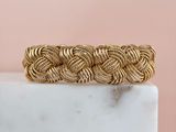 a close up of a gold braided bracelet on a marble block