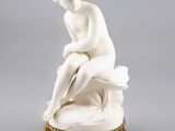une statue blanche représentant une femme assise sur une table
