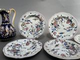 several plates and a pitcher sitting on a table with a vase in the background