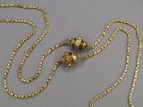 gold plated necklace with two beads and a chain on a gray surface