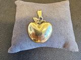 une photo d'un pendentif en forme de pomme en or posé sur un oreiller