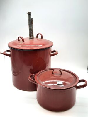 Deux pots rouges munis d'anses sont posés sur une surface blanche.