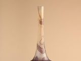 purple and white vase with a wooden handle sitting on a beige surface