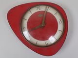 une horloge rouge au cadran blanc accrochée à un mur blanc