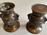 two metal vases sitting on a table with a white background