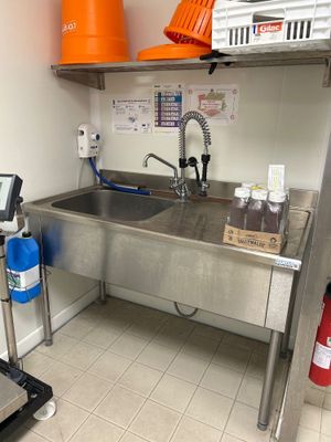 évier en acier inoxydable dans une cuisine professionnelle, avec des seaux orange accrochés au mur