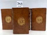 trois livres en cuir marron ornés de médaillons dorés, posés sur une surface blanche