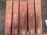 six livres rouges ornés de motifs dorés, posés sur une table