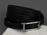 une ceinture en cuir noir avec une boucle argentée, posée sur un tissu blanc
