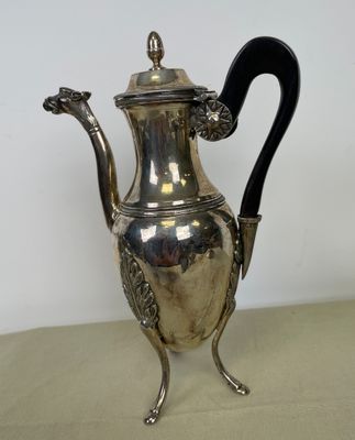 une cafetière en métal plaqué argent avec une poignée noire, posée sur une table