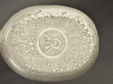 an old silver plate with a design on it on a black surface