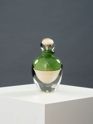 une bouteille en verre vert avec un bouchon doré, posée sur un socle blanc