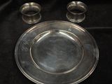 a silver plate and two silver cups on a black cloth