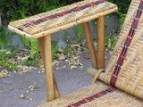a wicker chair with a table on it in front of a bush