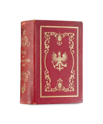 un vieux livre rouge avec des bordures dorées posé sur une surface blanche