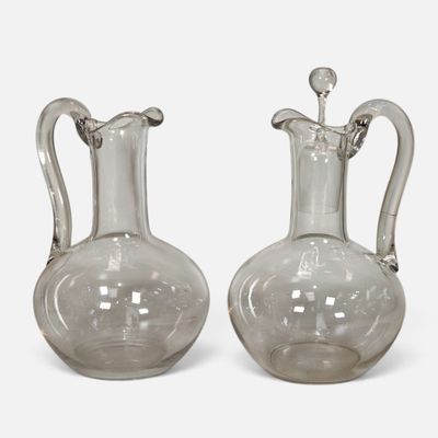 deux vases en verre transparent munis d'anses, posés sur un support blanc