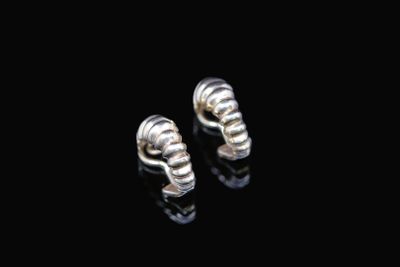 a pair of silver earrings sitting on top of a black surface