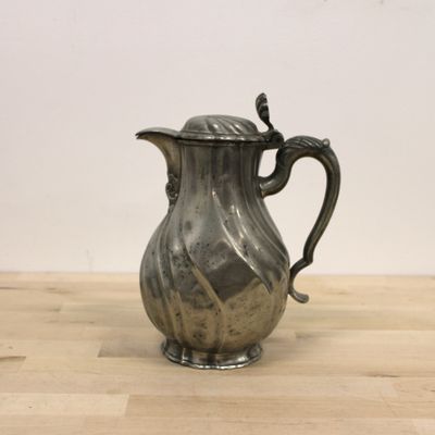 a silver pitcher on a wooden table with a white wall in the background
