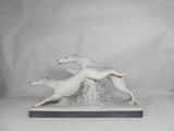 two figurines of greyhounds running on a white background