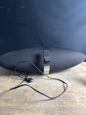 une enceinte noire posée sur une table en bois, avec un mur noir en arrière-plan