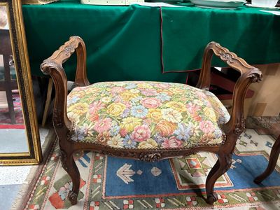 une chaise dont l'assise est recouverte d'un tissu à motifs floraux, placée devant un miroir