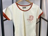 un t-shirt blanc avec une bordure orange, suspendu à un cintre dans la chambre