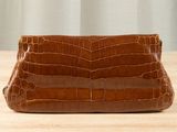 brown crocodile skin clutch bag on wooden table with curtain in background