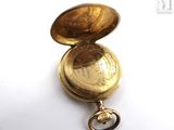 a gold pocket watch with a key on a white surface