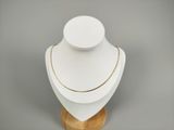 collier blanc et doré posé sur un support en bois, sur fond gris