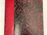 un vieux livre rouge et noir posé sur une table blanche