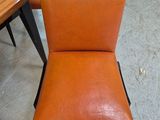 orange leather chair with black legs in a room with a table and chairs