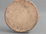 an old wooden plate sitting on a metal stand on a gray surface