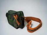 a green and orange bag and a brown strap on a white surface