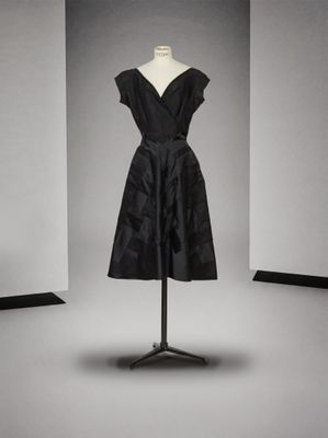 une robe noire posée sur un mannequin devant un mur blanc