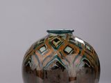 un vase brun et bleu posé sur une surface blanche