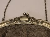 silver metal mesh purse hanging from a chain on a white wall