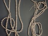 two pieces of silver beaded necklaces on a black surface