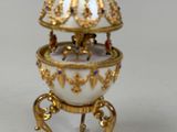 gold and white porcelain egg sitting on a stand on a white surface