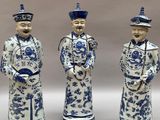 trois figurines bleues et blanches représentant des hommes coiffés d'un chapeau et vêtus d'une redingote