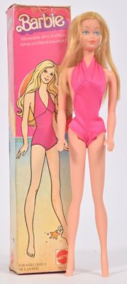 une poupée Barbie en maillot de bain rose, debout à côté d'une boîte de Barbie